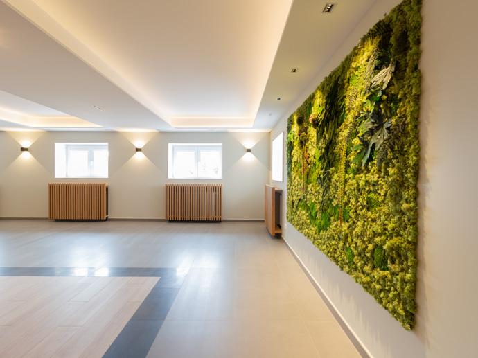 Se ve una sala amplia con una pared de plantas y musgos integrada, múltiples luces y ventanas